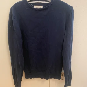 Marinblå tröja från Pier One - Snygg marinblå tröja från Pier One med rund hals och ribbade muddar. Tröjan är enkel och stilren, perfekt för dig som gillar klassisk look. Materialet är mjuk bomull och modellen har långärmade ärmar. 