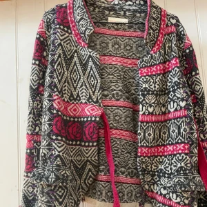 Mönstrad kofta från Odd Molly, st 1 - Unik kofta från Odd Molly med svart, vit och rosa mönster. Stickad i mjukt material med långa ärmar och snörning i midjan. Koftan har detaljerade grafiska och blommiga inslag, samt kontrastfärgade kanter. Perfekt för dig som gillar färg och mönster. Lovely knit i storlek 1. Finns några ullnoppror, som det lätt blir på ullplagg, annars i jättefint skick. 