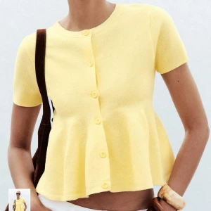 Gul blus med volang från Zara - Supersöt ljusgul blus från Zara med korta ärmar och rund hals. Blusen har knappar framtill och en volang nedtill som ger en skön och flowy vibe. Materialet är stickad syntet som känns mjukt mot huden. Perfekt för dig som gillar färg och vill sticka ut.