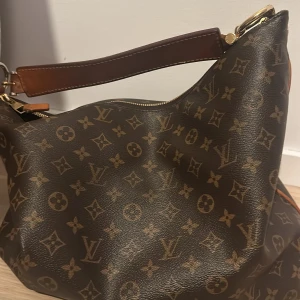 Louis Vuitton Monogram axelväska - Säljer en klassisk axelväska från Louis Vuitton med ikoniskt monogrammönster i brunt och beige. Väskan har en bred axelrem i läder och guldfärgade metalldetaljer. Perfekt för dig som vill ha en lyxig och tidlös accessoar.