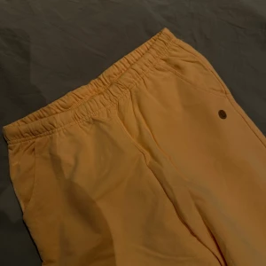 Ljusa  mjukisbyxor med resår - Snygga ljusgula mjukisbyxor med elastisk midja och muddar vid bensluten. Byxorna har sidofickor och en liten rund logga på höften. 