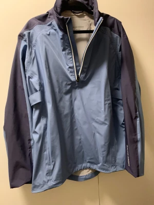 Blå vindjacka från Galvin Green - Snygg vindjacka från Galvin Green i två nyanser av blått med halv dragkedja framtill. Jackan har långärmade ärmar och sportig design med meshdetaljer på axlarna. Perfekt för dig som gillar stilren och funktionell ytterklädsel.ny pris ca 4500