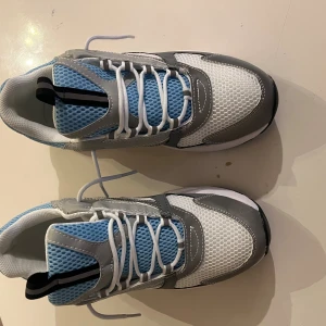 Grå och blå chunky sneakers - Chunky sneakers i grått, vitt och ljusblått med mesh- och syntetdetaljer. Skorna har vit snörning, svart och vit sula samt ventilerande mesh på ovandelen. Perfekta för dig som gillar sportig och modern stil.