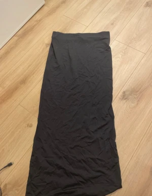 Svart tajt långkjol  - En svart långkjol i enkel och stilren design. Kjolen är rak och har en mjuk midja utan synliga detaljer. Perfekt för dig som gillar minimalistiska plagg och vill ha något som funkar till många olika looks.