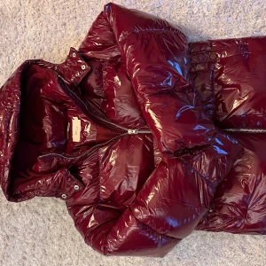 Vinröd pufferjacka från Nelly XS - Säljer en glansig vinröd pufferjacka från Nelly i storlek XS. Jackan har huva, dragkedja framtill och quiltad design som ger en cool vibe. Perfekt för kalla dagar när du vill vara både varm och snygg. Använd en gång, säljs pga för liten storlek.