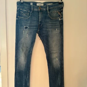 Replay Anbass Slim Fit – Storlek 32/32 - Säljer ett par blå jeans från Replay i modellen Anbass Slim Fit, storlek 32/32. Jeansen har en smal passform, klassisk femficksdesign och en mörkare blå tvätt med slitningar och detaljer som ger en snygg och modern look. De är använda en del men fortfarande i okej och fullt användbart skick utan några större skador. Nypris ligger vanligtvis på cirka 1 500–2 000 kr beroende på butik. Säljes då de inte längre kommer till användning.