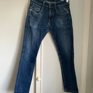 Replay Anbass jeans, stl 30 - Säljer ett par klassiska Replay Anbass jeans i blå denim. Jeansen har raka ben, snygga slitningar och detaljerade bakfickor. Perfekt passform och ikonisk Replay-knapp framtill. Materialet är mjukt och slitstarkt jeans.