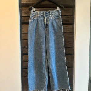 Levi's Ribcage jeans ljusblå - Klassiska Levi's ribcage crop jeans i ljusblå denim med raka, vida ben och hög midja. Byxorna har fem fickor, knappgylf och råa, fransiga benslut samt sydda veck framtill. Mjukt jeanstyg för skön passform. 