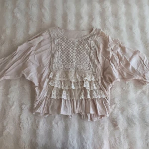 Romantisk volangblus med spetsdetaljer - Supersöt ljusbeige blus med ljusrosa underton, broderade spetsvolanger och virkade detaljer framtill. Blusen har vida ärmar och en lös passform. Pris kan diskuteras vid snabb köp💞