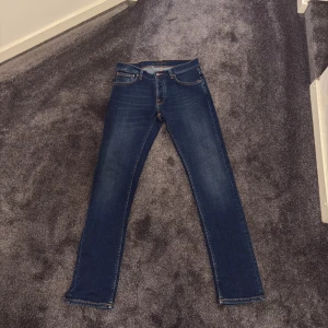 Nudie Jeans Grim Tim Indigo Myth - Snygga blå Nudie Jeans Grim Tim i färgen Indigo Myth. Jeansen har klassisk femficksdesign, orange sömmar och raka ben. Materialet är 99% bomull och 1% elastan för lite stretch. 