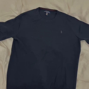 Mörkblå merinoull Polo Ralph Lauren S - Snygg mörkblå tröja från Polo Ralph Lauren i storlek S. Tillverkad i 100% ull med klassisk rund hals och diskret broderad logga på bröstet. Perfekt för dig som gillar stilrena och tidlösa plagg med premiumkänsla. Passar som S, XL i barnstorlek.