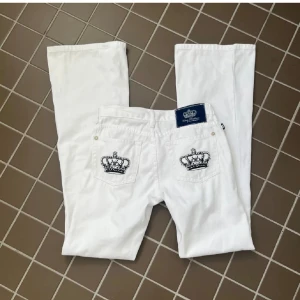 Vita jeansbyxor med kronbrodyr - Snygga vita jeansbyxor från Ed Hardy med broderade svarta kronor på bakfickorna och klassisk blå logotyp-patch i midjan. Raka ben och cool detalj med kontrastbrodyr gör dem till ett statement-plagg.