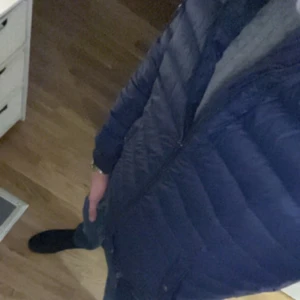 Mörkblå dunjacka Polo Ralph Lauren - Snygg mörkblå dunjacka från Polo Ralph Lauren med quiltad design och ribbade muddar. Jackan har dragkedja framtill, två fickor med tryckknapp och en ärmficka med dragkedja. Klassisk badge på ärmen och bomberjacke-inspirerad passform.