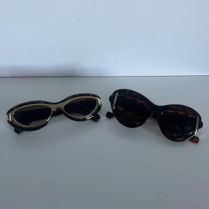 Två par bruna cat eye-solglasögon - Säljer två par trendiga solglasögon i cat eye-modell med brunmelerat sköldpaddsmönster. Ena paret har gulddetaljer runt bågen, det andra har guldfärgade detaljer på sidorna. Perfekta accessoarer för en cool look i solen.