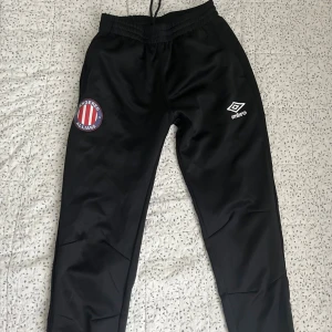 Svarta Umbro träningsbyxor XS - Svarta träningsbyxor från Umbro med Angered Allians-logga på ena benet och Umbro-logga på det andra.  Perfekta för fotboll eller träning.