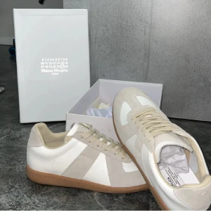 Helt nya populära sneakers  - Maison Margiela sneakers i vitt och beige med klassisk gummisula. Snygg design med paneler i skinn och mocka, rund tå och snörning. Perfekta för dig som gillar minimalistisk stil och exklusiva detaljer. Kommer med originalkartong.