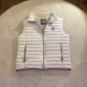 Vit dunväst från Colmar Originals - Snygg vit dunväst i strl S,52 från Colmar Originals med quiltad design och två praktiska fickor med dragkedja. Västen har en hög krage och coolt Colmar-märke på bröstet och ryggen. Perfekt för lager-på-lager och chill stil under kyliga dagar. Västen är i väldigt bra skick, med endast några små fläckar som man kan se på sista bilden. Hör av er vid fler frågor eller intresse!👍