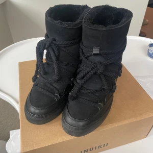 Svarta Inuikii boots med snörning - Säljer ett par svarta Inuikii boots i storlek 38. Skorna har grova snören, platt sula och är fodrade för extra värme. Tillverkade i mocka och skinn, perfekta för kalla dagar. Snygg och chunky design som sticker ut. INUKKI wege modell