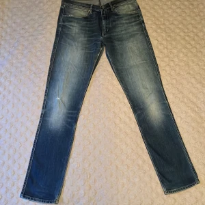 Blå Acne Studios jeans slim fit - Snygga blå jeans från Acne Studios i slim fit med klassisk femficksdesign. Jeansen har slitningar och en mindre reva på vänster ben för en cool, använd look. Materialet är bomull och passformen är normal. Perfekt för dig som gillar stilrena och trendiga jeans. Storlek 32/32