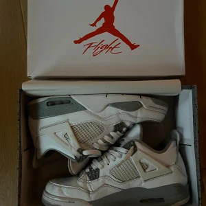 Nike Air Jordan 4 Oreo - Nike Air Jordan 4 Oreo med vit ovandel i skinn, grå detaljer och stänkmönstrad mellansula. Klassisk meshpanel på sidorna, röda Jumpman-loggor på plös och sula. Snygg retro vibe och ikonisk siluett, perfekt för dig som vill sticka ut.