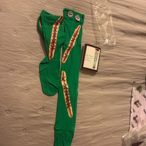 Gröna lårhöga strumpor Leg Avenue - Säljer ett par gröna lårhöga strumpor från Leg Avenue med coolt Frankenstein-inspirerat sår- och bultmönster. Perfekta för halloween eller temafest! Opaque material och detaljer som ser ut som stygn och metallbultar upptill.