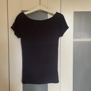 Mörkgrå topp med öppen rygg Gina Tricot - Svart, tight topp från Gina Tricot i storlek XS. Modellen har korta ärmar och en djup, öppen rygg som ger en snygg och edgy look. Tunn och mjuk bomullskvalitet, perfekt för att styla med jeans eller kjol. Enkel och stilren design.