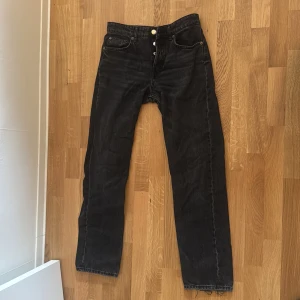 Svarta raka jeans från Zara - Svarta jeans från Zara med raka ben och klassisk femficksdesign. Jeansen har silverfärgade knappar med logga och är tillverkade i ett slitstarkt bomullsmaterial. Snygg, enkel look som funkar till allt och har en normal passform. Jeansen säljs inte längre men om nån har koll på trender så har de dom som alla köpte för nått år sedan 