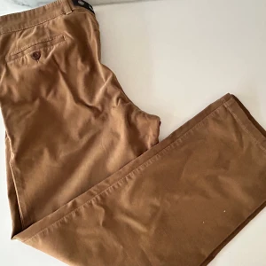 Bruna chinos från Brax i bomull - Snygga bruna chinos från Brax med klassisk rak passform och diskreta bakfickor med knapp. Byxorna är tillverkade i mjuk bomull med lite stretch för extra komfort. Från Tyska kvalitetsmärket Brax (säljs bland annat på NK)  Storleken för byxorna på etiketten är 36/30 (US) och motsvarar enligt AI en svensk storlek 46/30.  Använda men ännu i skick. Nypris 1500 kr.