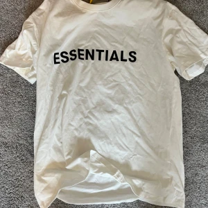Vit Essentials t-shirt med tryck - Vit t-shirt från Essentials med svart tryck på bröstet. Klassisk rund halsringning och korta ärmar. Tillverkad i mjuk bomull för en skön känsla. Perfekt basic-plagg med clean look och oversized passform.