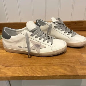 Golden Goose Superstar skor  - Säljer mina Golden Goose Superstar skor då dom var för små!  De är i vitt skinn med grå mockadetaljer och grå snörning. Klassisk stjärna på sidan i ljusgrå mocka och grå hälkappa. Platt sula och rund tå. Snygg och trendig modell med coola vintage-vibbar.        Skorna är endast provade så dom är i mycket bra skick! .Box medföljer tyvärr inte!                       Skriv gärna om du har en fråga!                           MVH Nils