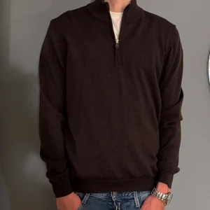 Brun stickad half zip från Oscar Jacobson - Snygg brun stickad tröja från Oscar Jacobson med half zip och hög krage. Perfekt för lager-på-lager och passar till jeans eller chinos. Tröjan har lång ärm och ribbade muddar för en clean look. 100% mjuk ull 