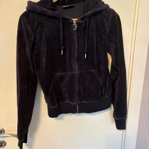 Mörkblå velour hoodie Juicy Couture - Säljer en mörkblå hoodie från Juicy Couture i mjuk velour med huva och snörning. Tröjan har dragkedja med Juicy-logga, två fickor fram och ribbade muddar. Perfekt för chill dagar och har en klassisk streetstil.