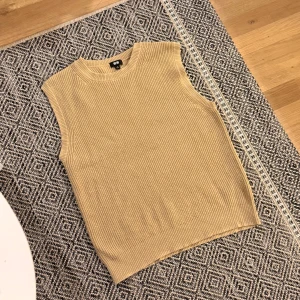 Beige stickad väst från Uniqlo - Ribbstickad beige väst från Uniqlo med rund halsringning och ärmlös design. Perfekt att styla över en skjorta eller t-shirt för en trendig lager-på-lager-look. Enkel och stilren modell som passar till mycket.