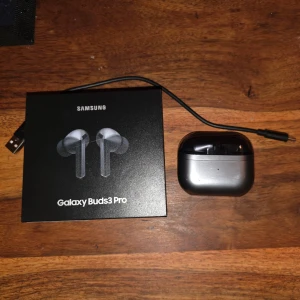 Galaxy Buds3 Pro - Samsung Galaxy Buds3 Pro trådlösa hörlurar med laddningsetui och USB-C kabel. Hörlurarna och etuiet ser ut att vara i mycket gott skick utan synligt slitage. Levereras med originalförpackning. Perfekt för musik, samtal och aktiv brusreducering.