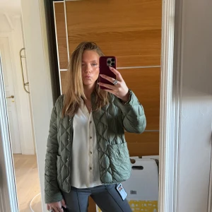 Olivgrön quiltad jacka - Snygg olivgrön quiltad jacka med tryckknappar och två stora fickor framtill. Jackan har en rak passform och är lätt vadderad, perfekt för övergångssäsonger. Stilsäker och enkel att matcha med olika outfits.