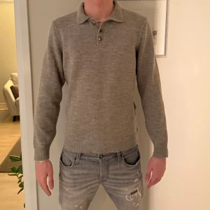 Grå stickad polotröja från Studio - Snygg grå stickad polotröja från Studio i storlek M. Tröjan har en klassisk krage med två knappar framtill och långa ärmar. Perfekt för lager-på-lager och chill höst- och vinterstil. Enkel att matcha med jeans eller chinos.