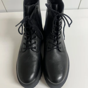 Svarta boots från ELLA of Sweden - Tuffa svarta boots från Ella of Sweden i skinn med grov sula och snörning framtill. Dragkedja på sidan för enkel påtagning och rund tå. Perfekta för dig som gillar en chunky look och vill ha något som sticker ut.Lätt fodrade på insidan.