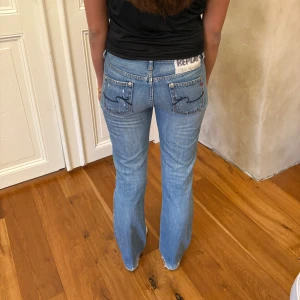 Replay ljusblå bootcut jeans - Säljer ett par ljusblå jeans från Replay med bootcut passform och låg midja. Jeansen har klassiska fem fickor, snygga detaljer på bakfickorna och en liten Replay-logga på linningen. Perfekta för dig som gillar en avslappnad och trendig stil.