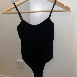 Svart ärmlös linnetopp med smala band - Säljer en svart linnetopp med smala axelband och djup rundad halsringning. Toppen är ärmlös och har en tight passform som framhäver siluetten. Perfekt att styla med jeans eller kjol för en clean look.