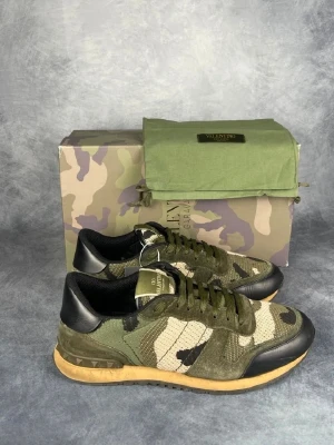 Valentino Garavani Rockrunner sneakers - Snygga Valentino Garavani Rockrunner sneakers med camouflage-mönster i grönt, beige och svart. Skorna har platt sula, rund tå och snörning. Materialmix av mocka, skinn och textil. Ikoniska nitar på hälen och coola detaljer. Perfekt för dig som gillar streetstyle och designer. Hör av er vid frågor✅️