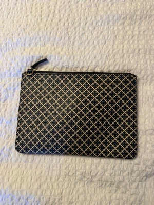 Marlene Birger väska  - Snygg svart kuvertväska med diskret rutigt mönster och guldfärgad dragkedja. Väskan är tillverkad i skinnimmitaion och har en beige insida. Från by Marlene Birger, band tillkommer inte. 