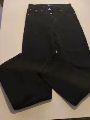 Svarta jeans - Säljer ett par klassiska svarta jeans med raka ben och knappgylf. Byxorna har fem fickor och snygga nitar vid fickorna. Perfekta för dig som gillar tidlös stil och vill ha ett par jeans som funkar till allt.