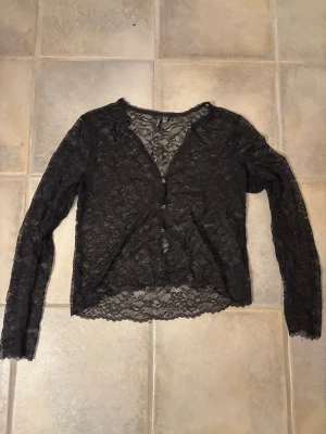 Svart spetskofta från Vero Moda - Hej!👋 Jag säljer en svart, genombruten spetskofta från Vero Moda✌️ Koftan har långa ärmar, v-ringad hals och knäppning framtill med små knappar🔥Perfekt för dig som vill ha en snygg layering-piece med lite extra edge🙌 Meddela gärna vid frågor💗