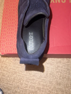 Mörkblå slip-on sneakers från Footlight - Säljer ett par mörkblå slip-on sneakers från Footlight med snygga blå detaljer och små glittriga prickar på ovansidan. Skorna har en platt svart sula och är tillverkade i mocka för en mjuk och lyxig känsla. Perfekt för dig som gillar stilrena och bekväma skor. Aldrig använda 