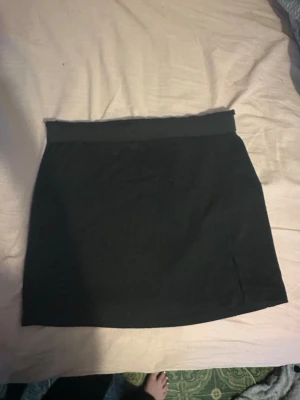 Svart kortkjol i bomull - Enkel svart kortkjol i mjukt bomullstyg. Kjolen har en rak passform och bred linning upptill för en bekväm känsla.Kjolen har även ett slitt längst ner på ena sidan. Perfekt att matcha med en crop top eller hoodie för en chill look.