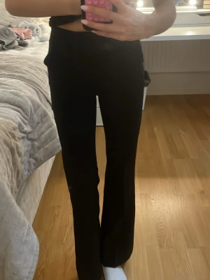 Svarta bootcut kostym byxor med hög midja - Säljer ett par svarta bootcut kostym byxor med hög midja. De har en snygg och enkel design med raka ben som blir lite vidare nedtill. Materialet känns mjukt och, perfekt för dig som gillar bekväma och stilrena byxor.