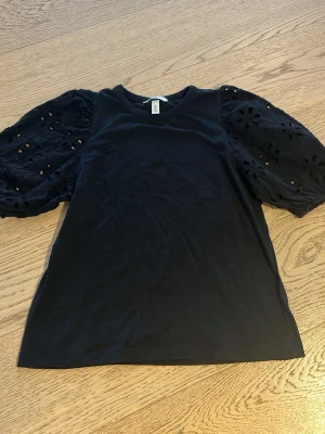 Svart blus med puffärmar från H&M - Säljer en svart blus från H&M med puffiga, korta ärmar i broderad bomull och blommönster. 