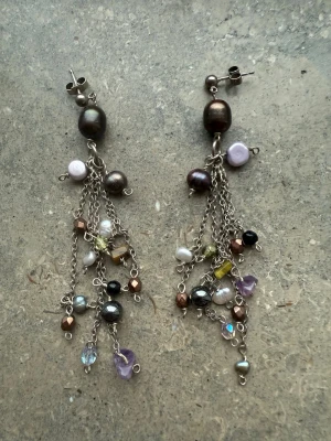 Färgglada statementörhängen med pärlor - Unika örhängen med silverfärgade kedjor och massor av små pärlor i olika färger som lila, svart, vit, brun och gult. Hängande design med mix av glansiga och matta pärlor samt små stenar. Perfekta för att lyfta vilken outfit som helst.