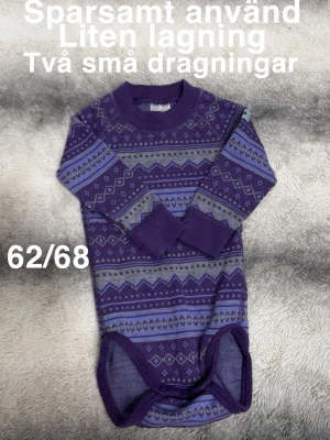 Lila mönstrad ullbody 62/68 - Säljer en långärmad body i lila och grå toner med snyggt geometriskt mönster. Perfekt för dig som gillar färg och mönster på barnkläder. Mjuk och skön. Tryckknappar i grenen för enkel påklädning.🌸 Sparsamt använd. Liten lagning och två små dragningar som blev på första användning. Storlek 62/68