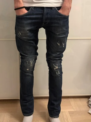 Dondup jeans - Säljer ett par mörkblå skinny jeans med snygga slitningar på framsidan. Jeansen har klassisk femficksdesign, smal passform och gul kontrastsöm på bakfickorna. Perfekta för dig som gillar en modern och avslappnad stil.